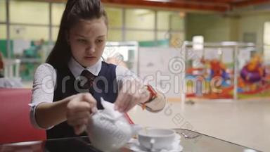 在<strong>学校食堂</strong>休息。 一个十几岁的女孩把茶从水壶里倒入杯里。